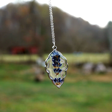 Lavender Sprig Necklace held in hand in a field setting, showcasing the pendant design, craftsmanship, and natural outdoor lifestyle aesthetic